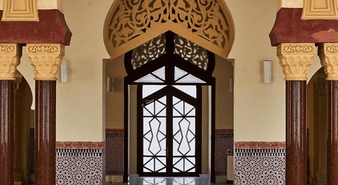 Decorative arched doorway with geometric glass pattern, ornate columns, and detailed tilework in an indoor setting.
