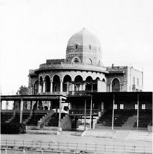 Black and white image of a streetcar turning along a curved track, with historical buildings lining a wide, empty road.