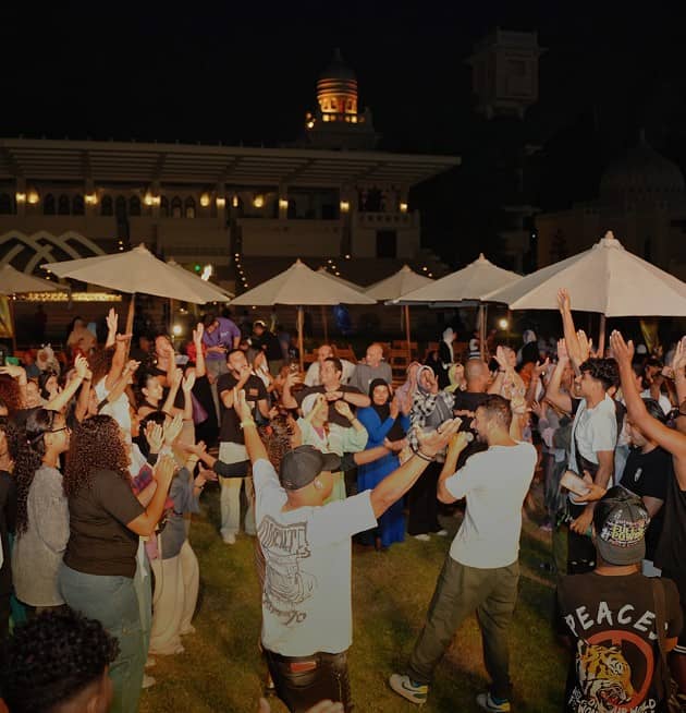Large white sign reads '120 Years of Legacy Reimagined' in English and Arabic in front of a historic building with arched windows and red-and-white striped stonework.