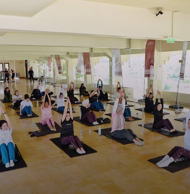 Large white sign reads '120 Years of Legacy Reimagined' in English and Arabic in front of a historic building with arched windows and red-and-white striped stonework.